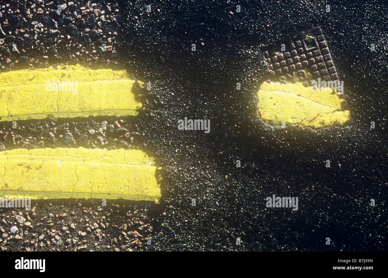 Detail from above of bright double yellow lines laid down twice with patch of asphalt lying over them and small metal GAS cover Stock Photo