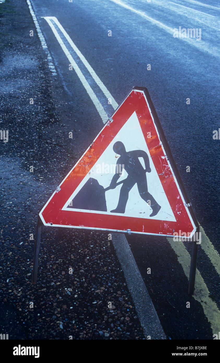 Damp sunlit black road and pavement with red and white Roadworker sign and double yellow lines Stock Photo