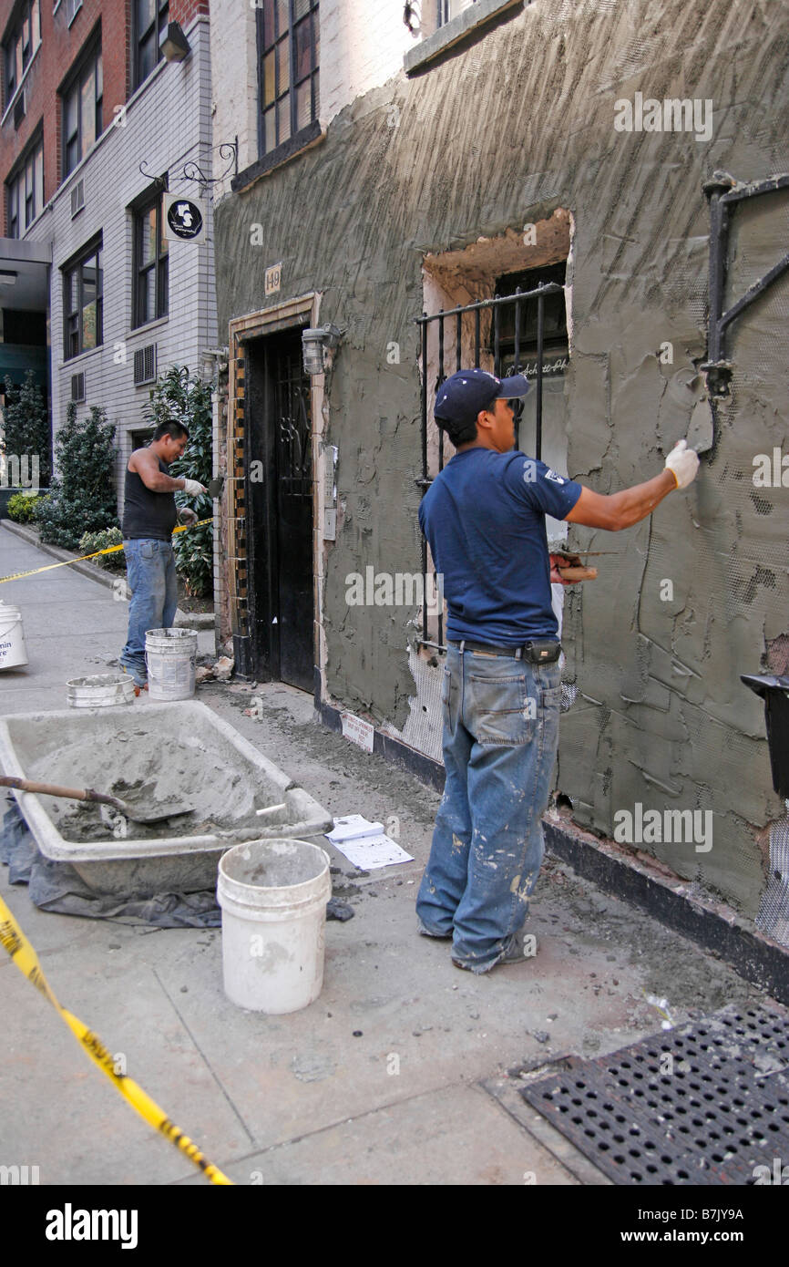 Two workers repair the exterior wall of a combination commercial and apartment building in an urban city Stock Photo