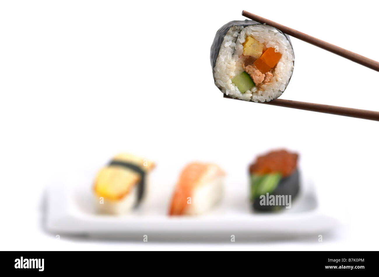 Japanese food: delicious Futomaki hold with chopsticks and selection of three nigiri shushes isolated on white background Stock Photo