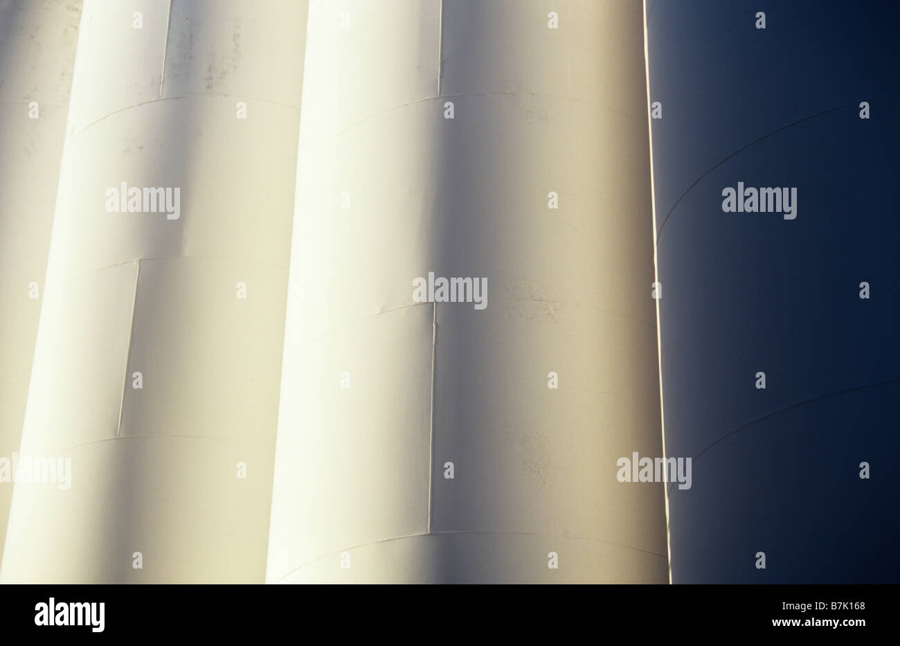 Low sunlight glancing across closely grouped white painted large industrial or petroleum storage tanks Stock Photo