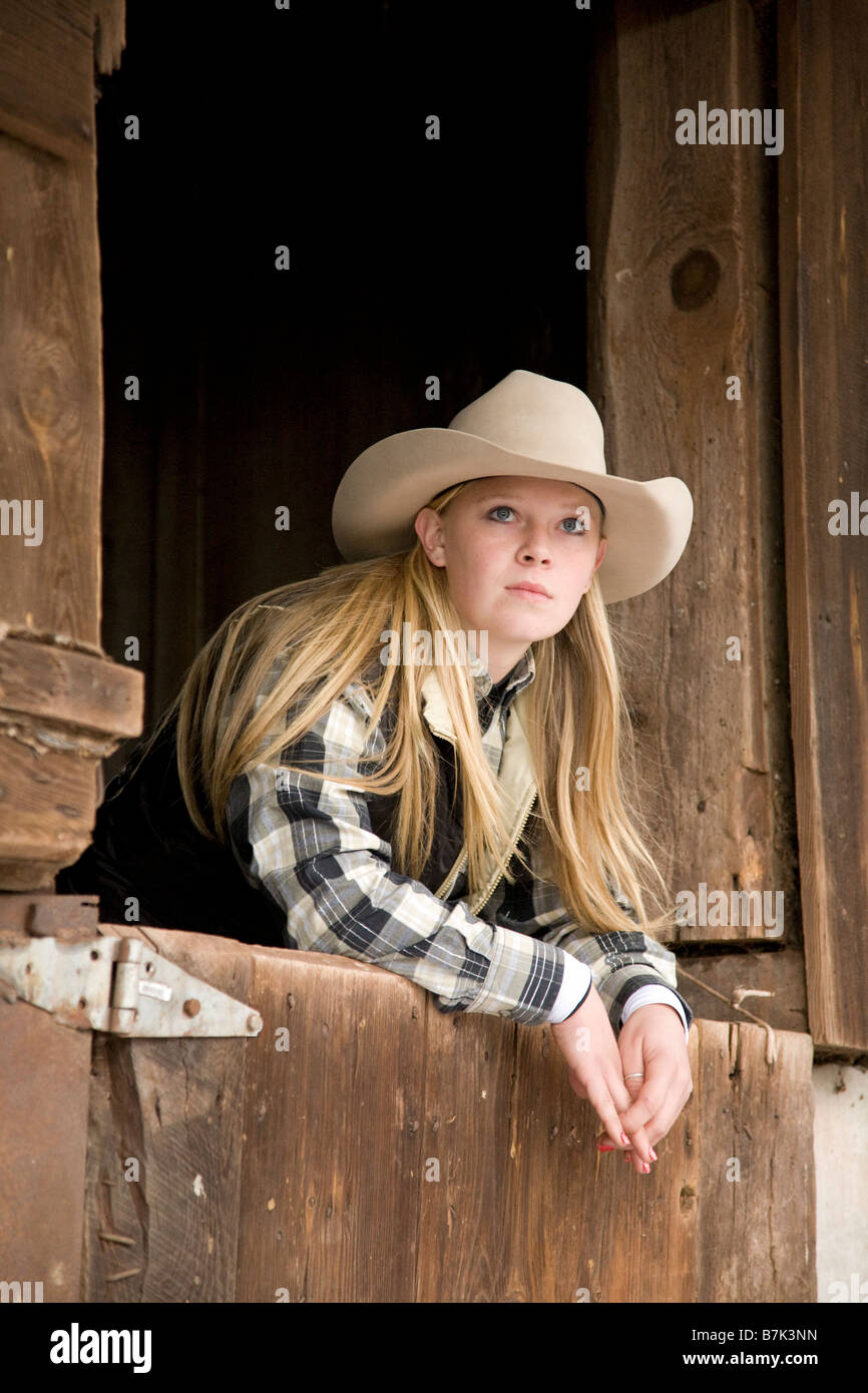Teenage Cowgirl Leaning On Stall Door Of Old Wooden Ba
