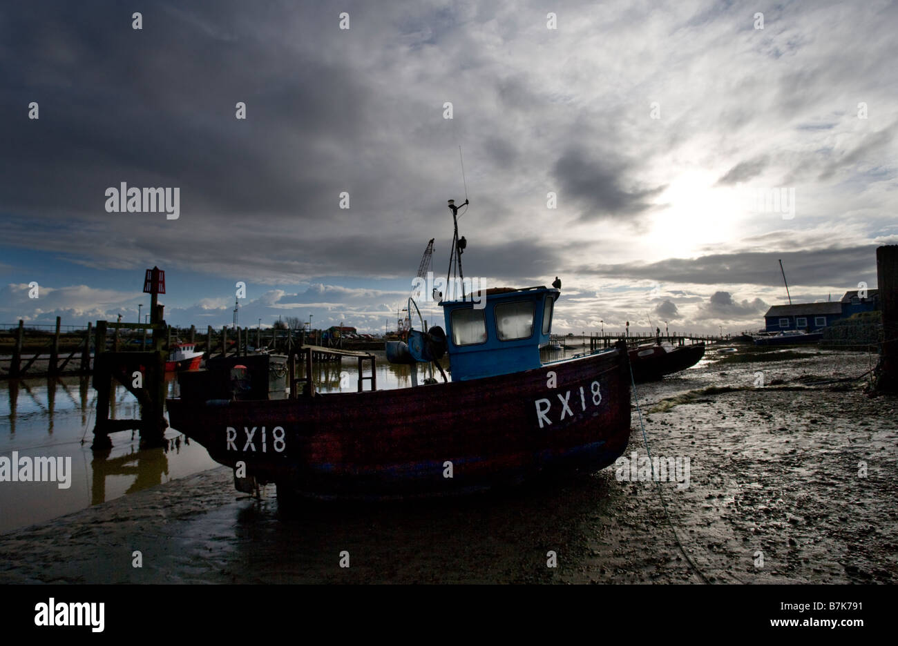 Silhouetted fishing boats beached at low tide on the banks of the estuary of the river Rother at Rye Sussex UK Stock Photo