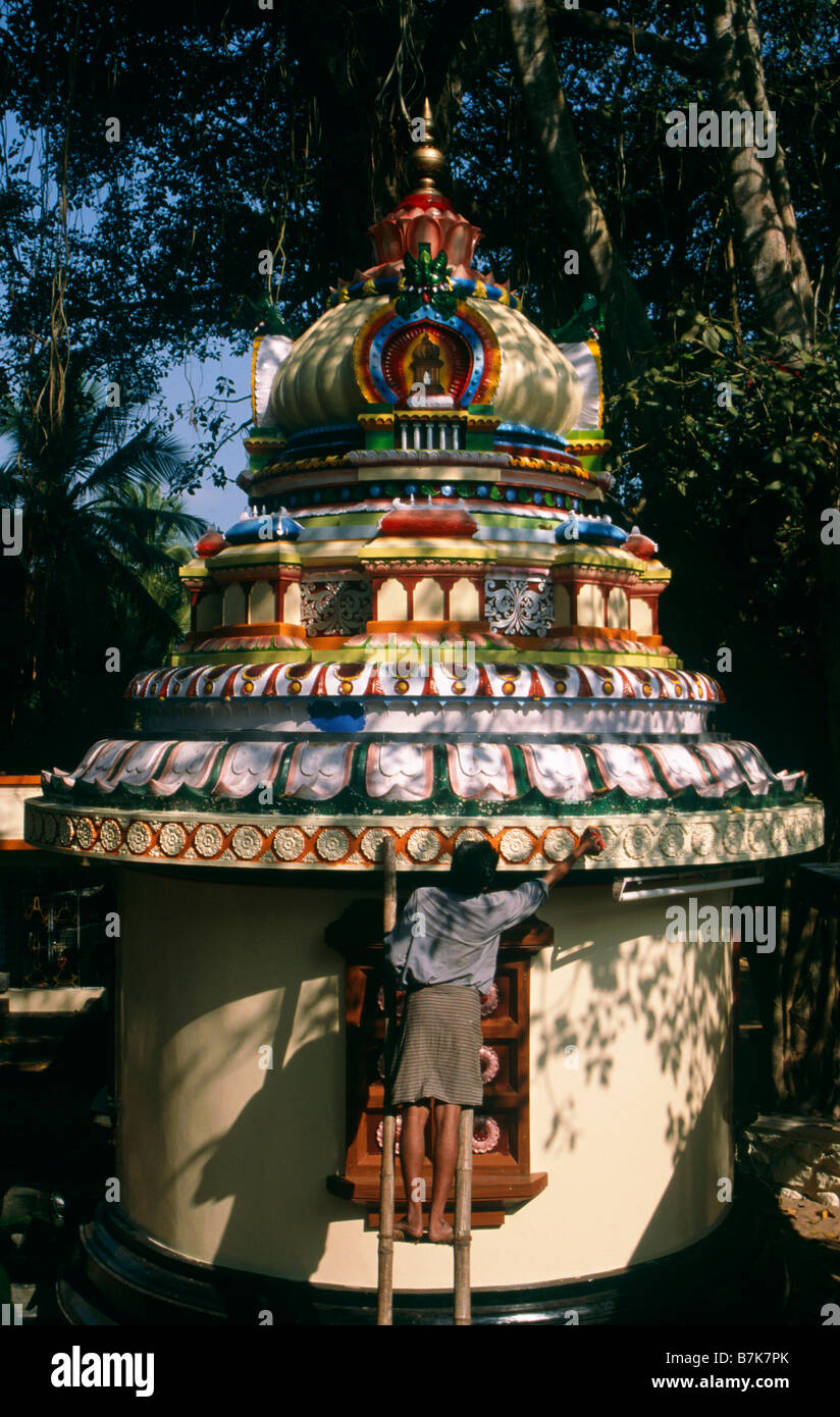 Man on ladder painting shrine Bright colours SHRINE KERALA INDIA Stock