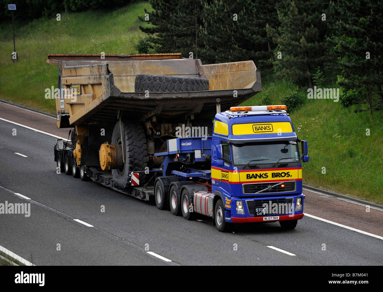 Banks Volvo FH heavy haulage truck carrying a giant dump truck wide abnormal load on the motorway Stock Photo