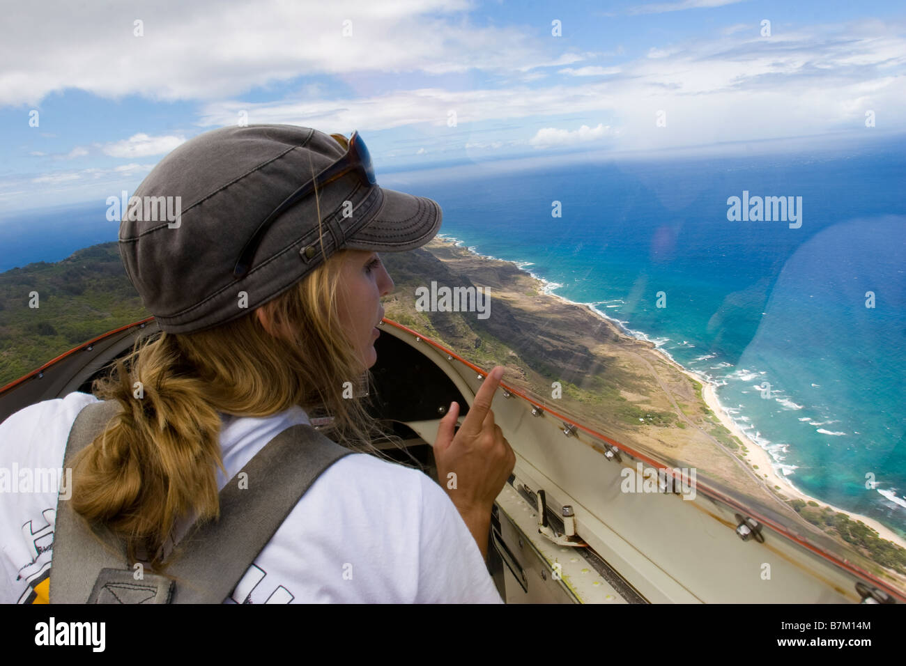 Female pilot in glider airplane flying over coastline, pointing to landmarks along north coast of Oahu Hawaii, near Dillingham Stock Photo