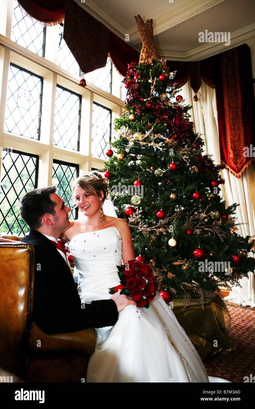 Bride and Groom at Xmas time winter wedding day cuddle in arm chair in front of Xmas Christmas tree warm and festive wedding day Stock Photo