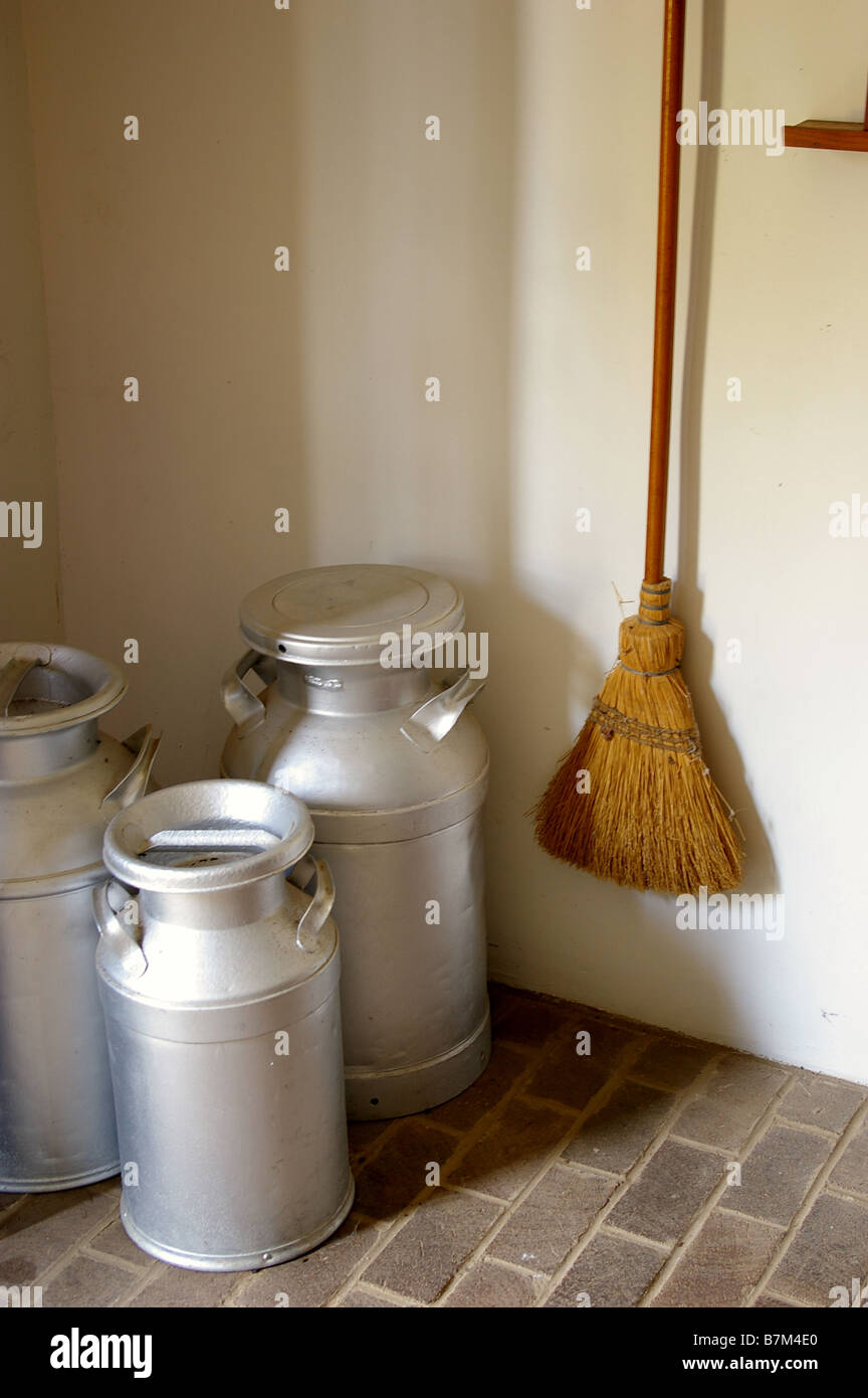 Milk can with broom hanging on wall Stock Photo