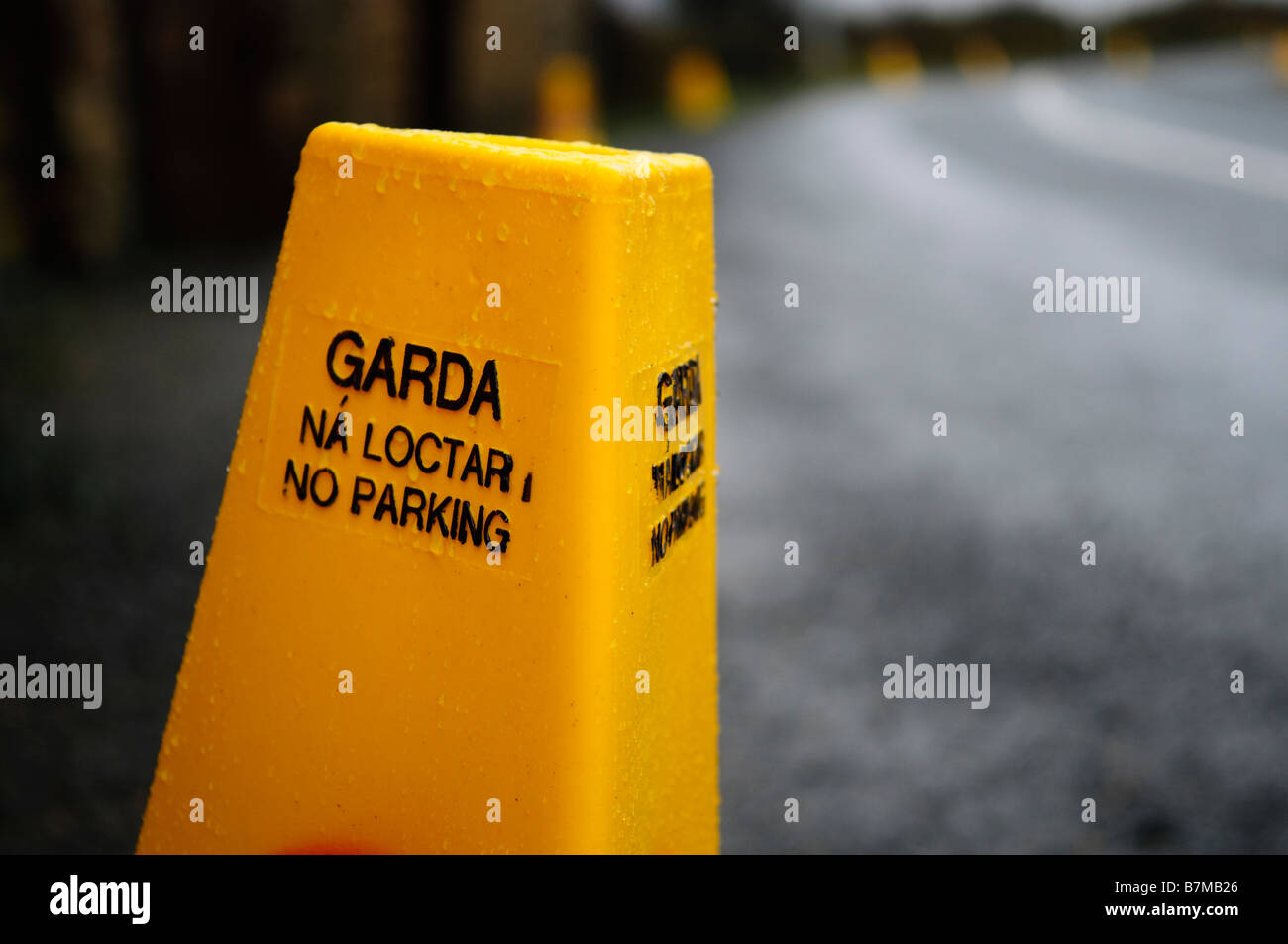 Yellow Garda traffic cones with bilingual sign in english and gaelic - 'No Parking. Ná loctar'. Wet road and rain. Stock Photo