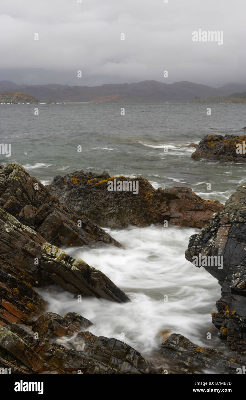 White waves between rocks and view across Sound of Arisaig on a grey ...
