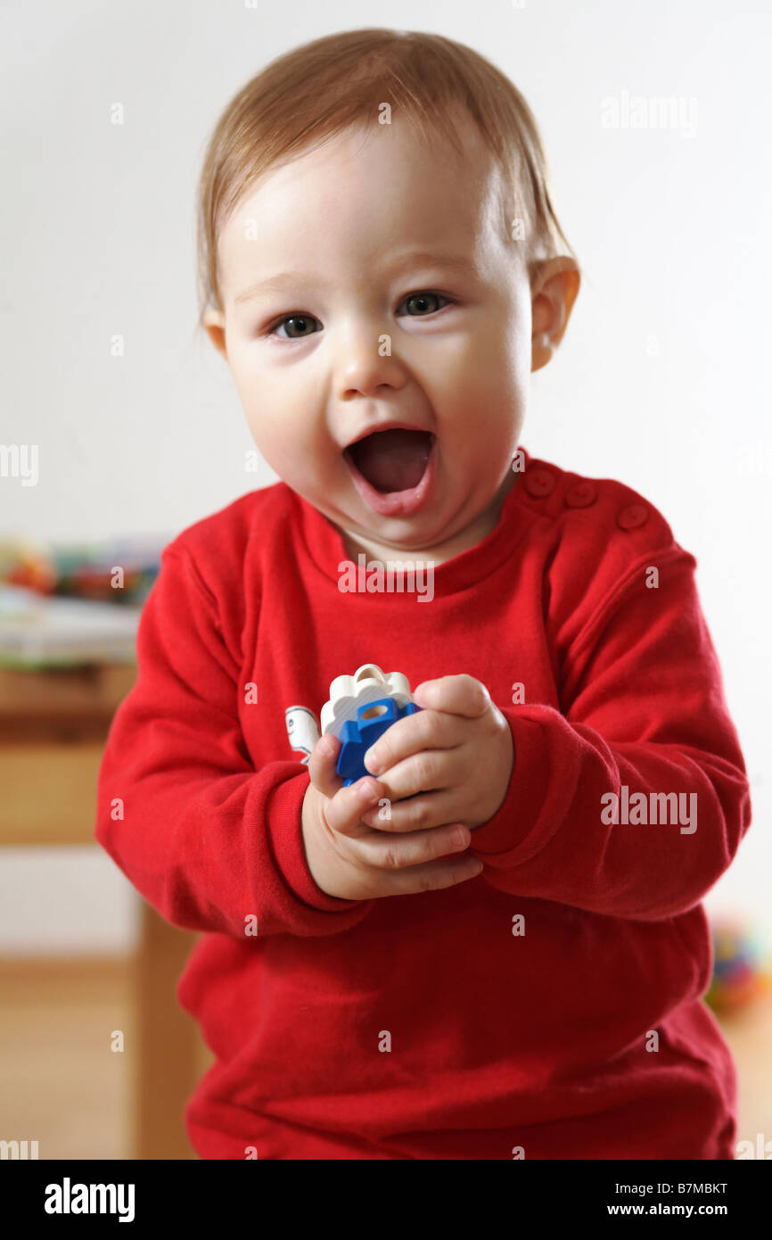 Child (12-18 months) toys in hand, shouting at the camera. Stock Photo