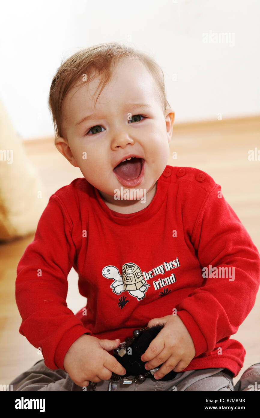 Child (12-18 months) sitting on the floor, shouting at the camera. Stock Photo