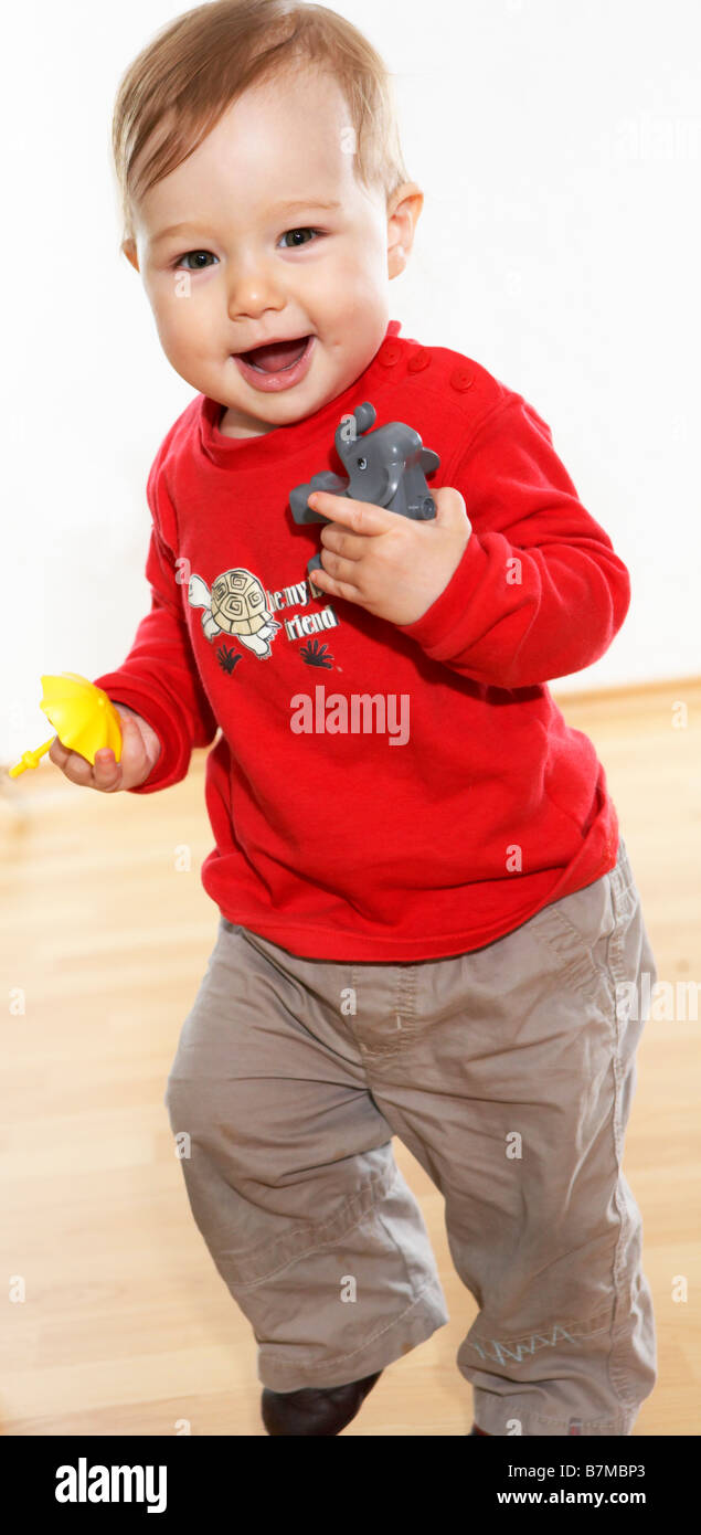 Child (12-18 month) running with toys in hand. Laughing at the camera. Stock Photo