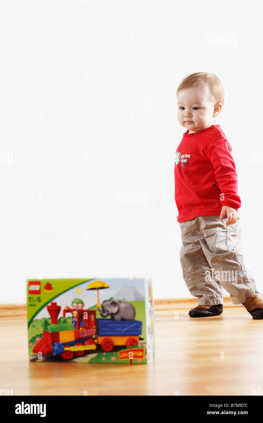 Child (12-18 months) standing in front of box of new toys. Stock Photo