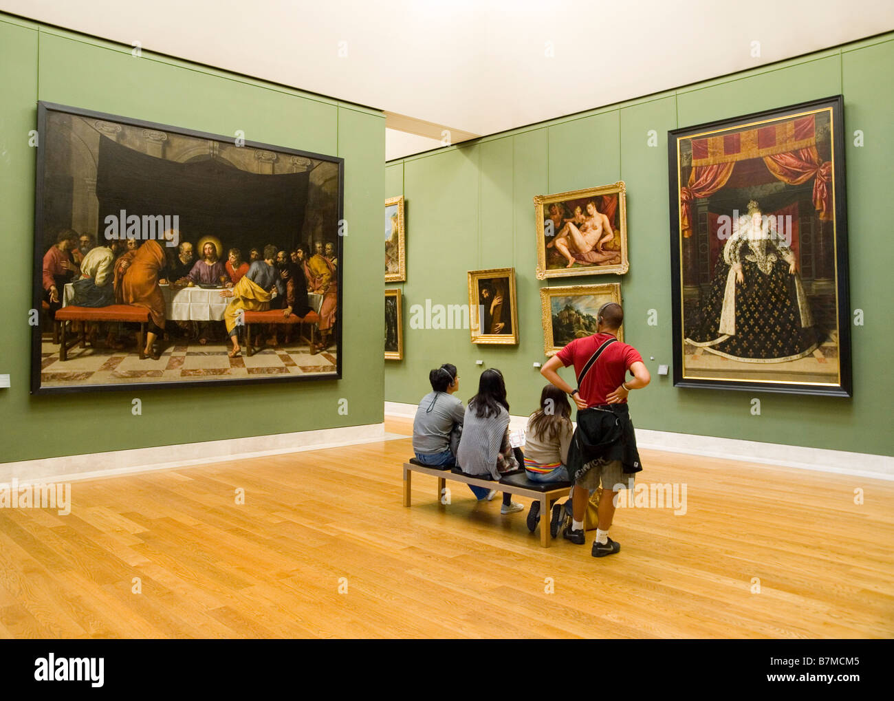 People sitting looking at paintings in a gallery in the Louvre Museum