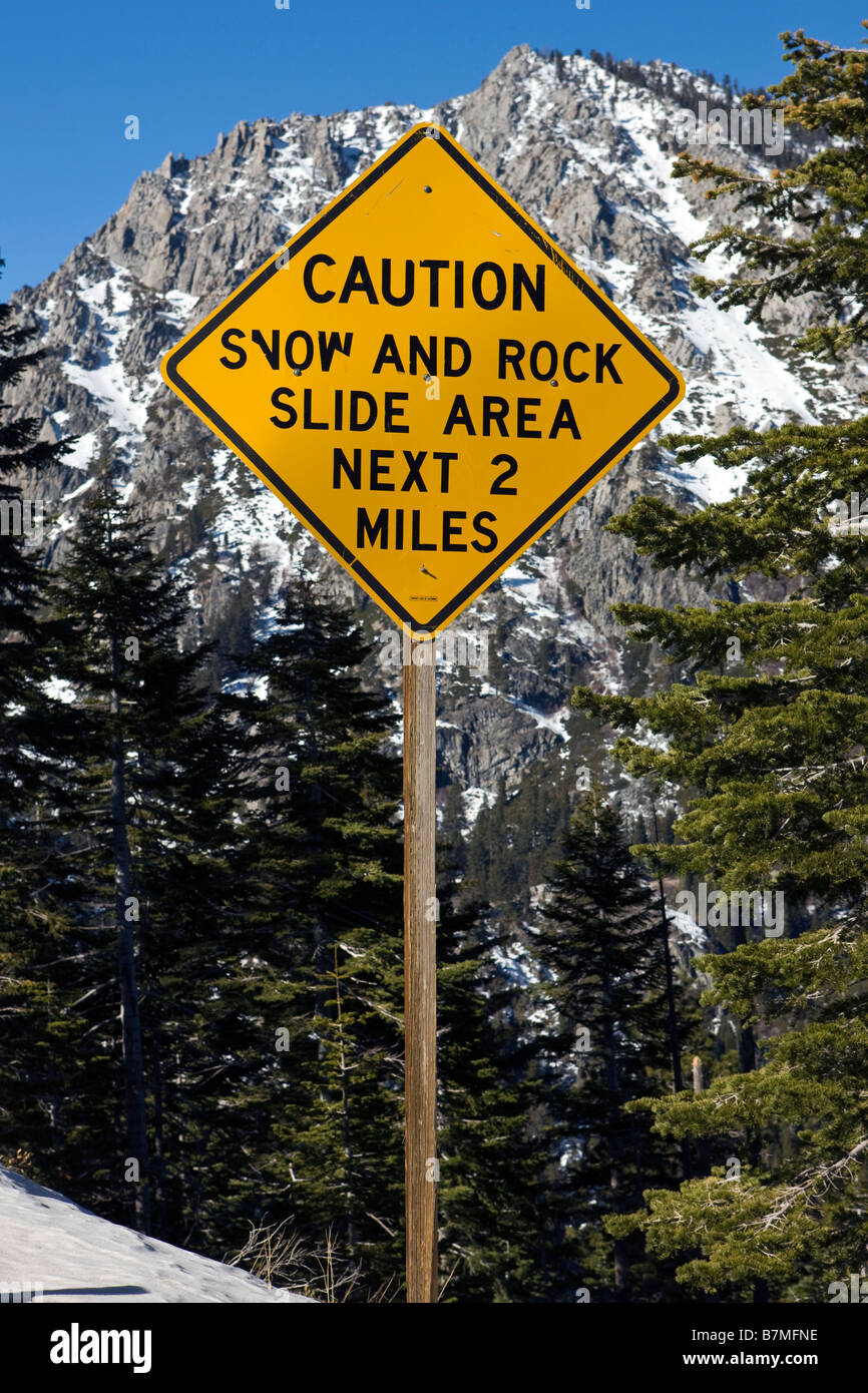 A road sign warning of snow and rock slides in front of a snow covered mountain Lake Tahoe California Stock Photo