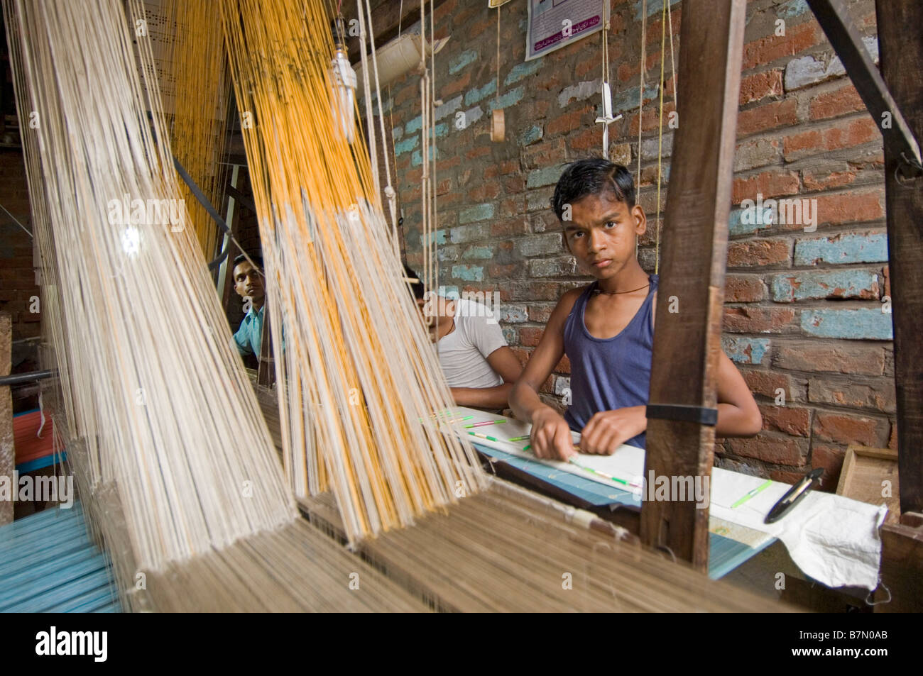 Child labour in the small textile factories of Varanasi - a young boy working for a pittance making silk saris on a loom. Stock Photo