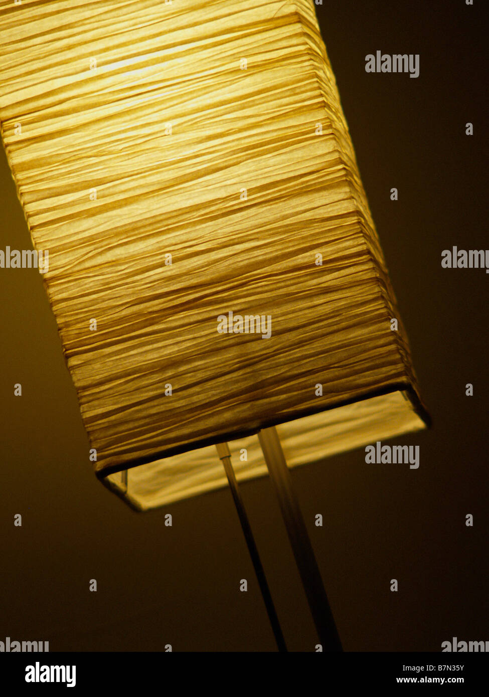 Small illuminated lamp with wrinkled paper shade against dim background. Stock Photo