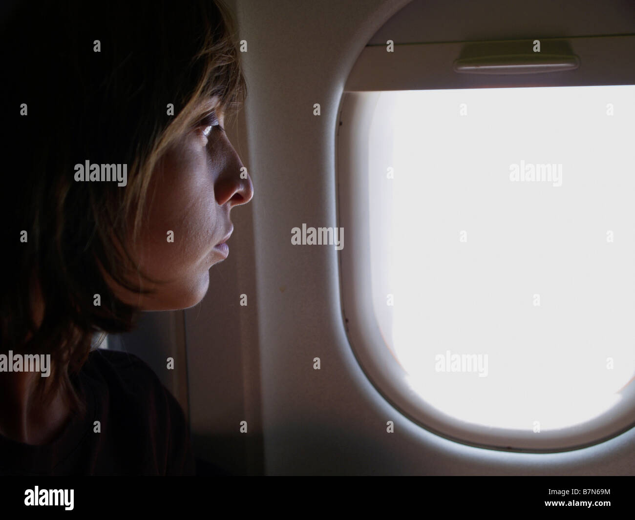 Woman looking apprehensively out airplane window during transatlantic flight. Stock Photo