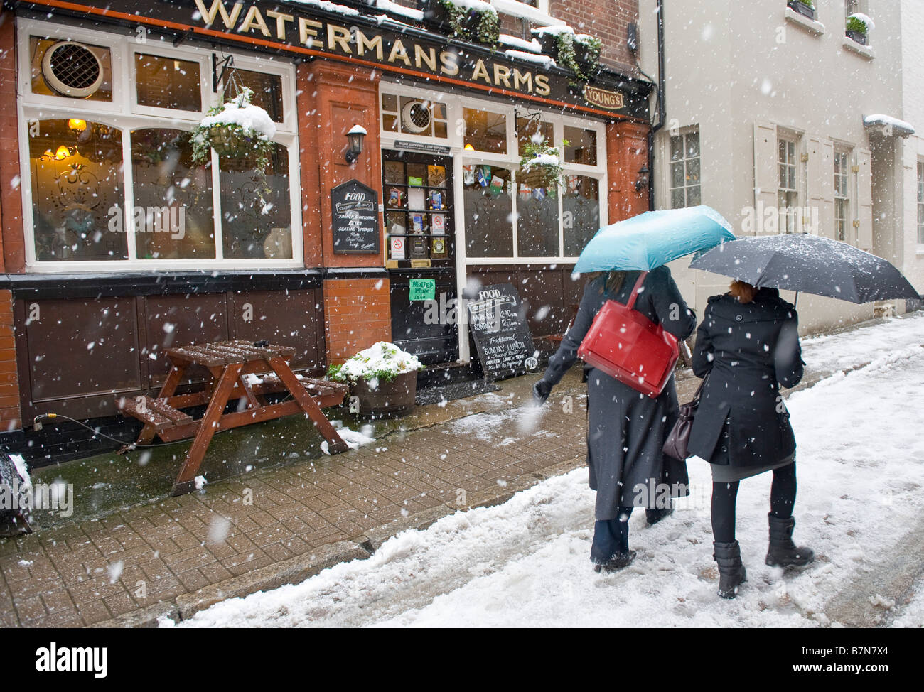 Two women passing in front of Waterman's pub under heavy snowfall, Richmond upon Thames, London, UK Stock Photo