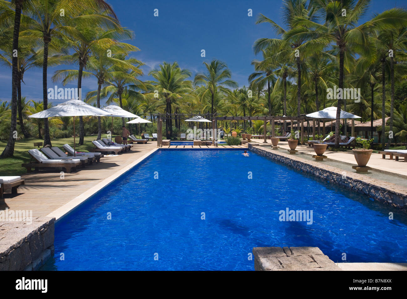 Birght blue swimming pool fringed by palm trees in grounds of hotel in