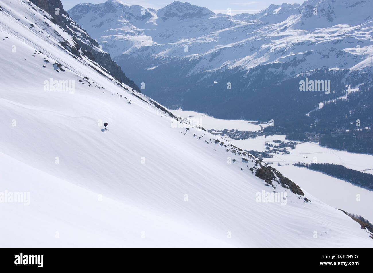 Ski alpinist descends a slope in direction of frozen Lake Sils and Lake Silvaplana. Graubunden, Switzerland Stock Photo