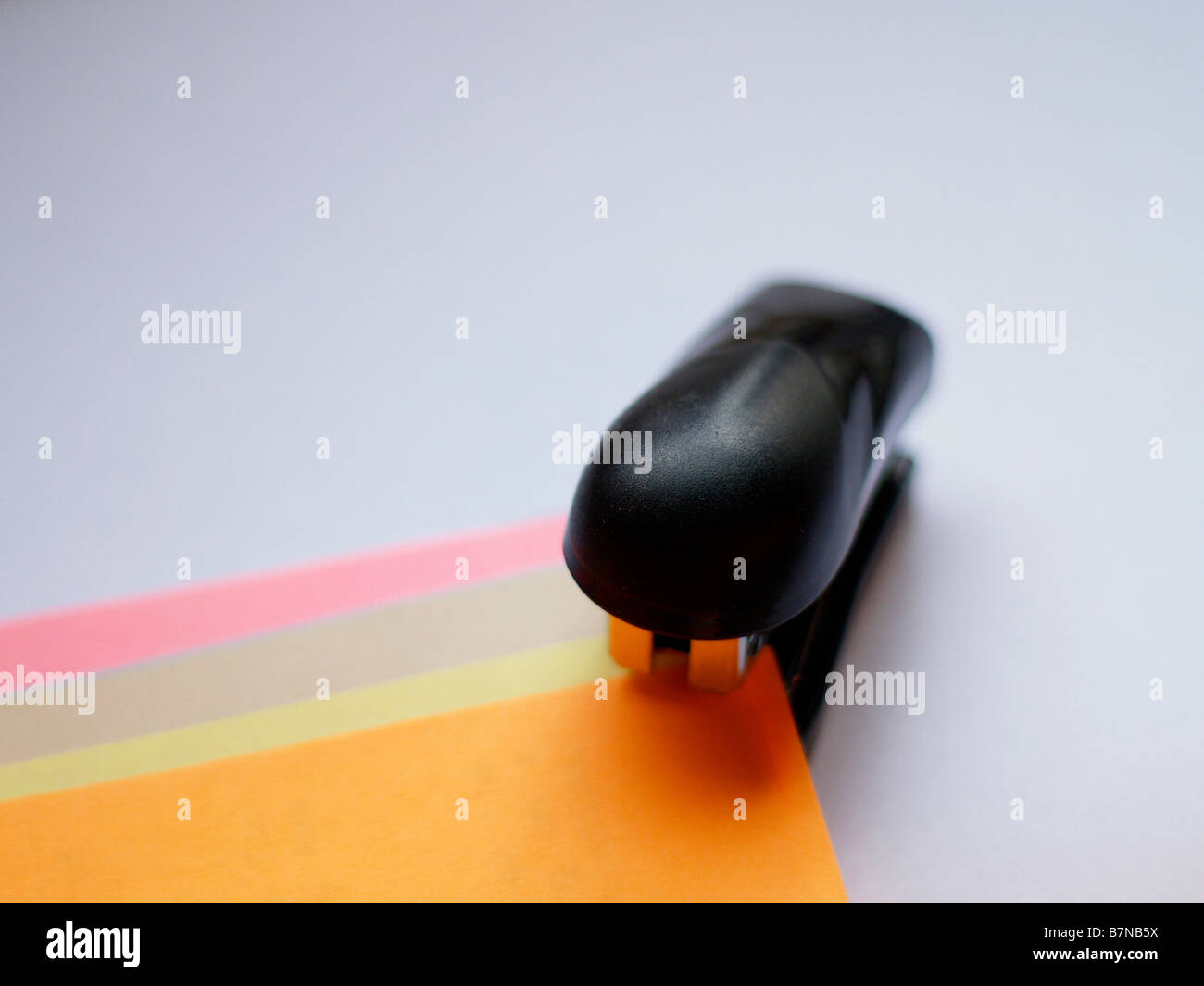 Small stapler about to staple multi-colored sheets of paper in earth tones, shallow focus, isolated background. Stock Photo