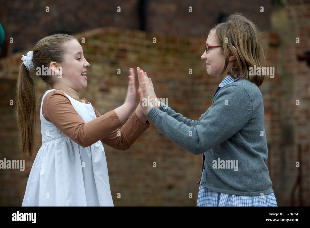 Children in Victorian costume, play clap hands in the playground, a traditional game. Stock Photo