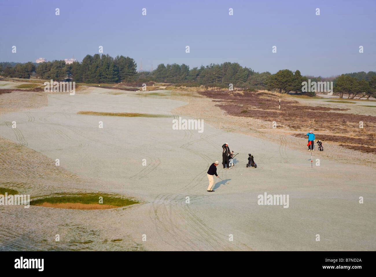 Three golfers playing golf in winter when the ground and golf course is