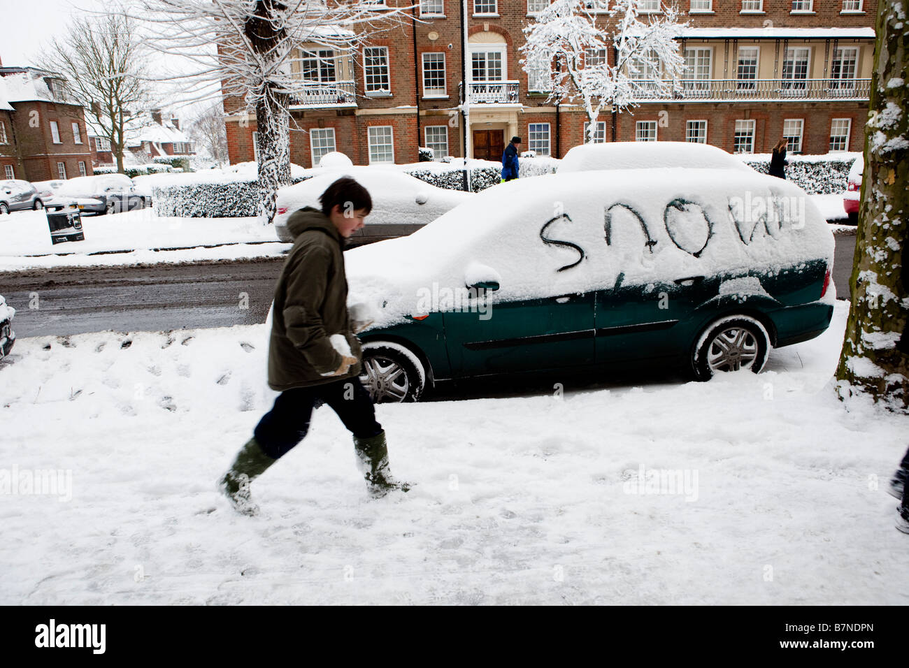 A teenager walks past a car where someone has written the word Snow in the snow Stock Photo