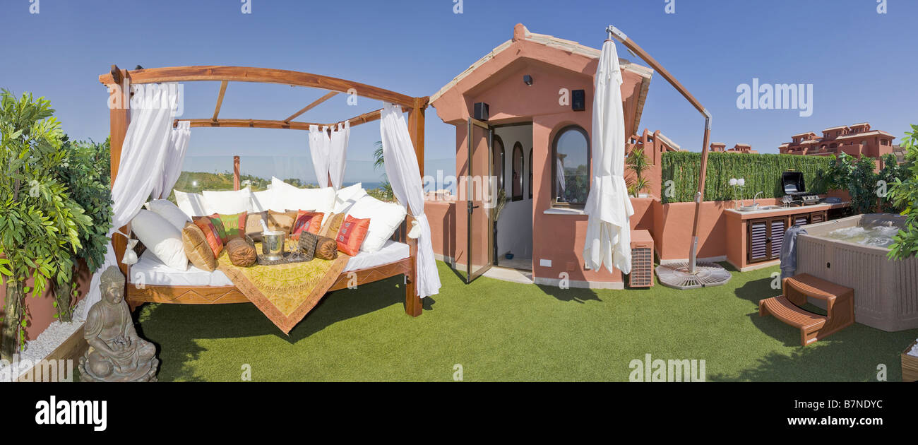 White cushions on large comfy swing seat on roof garden with fake grass