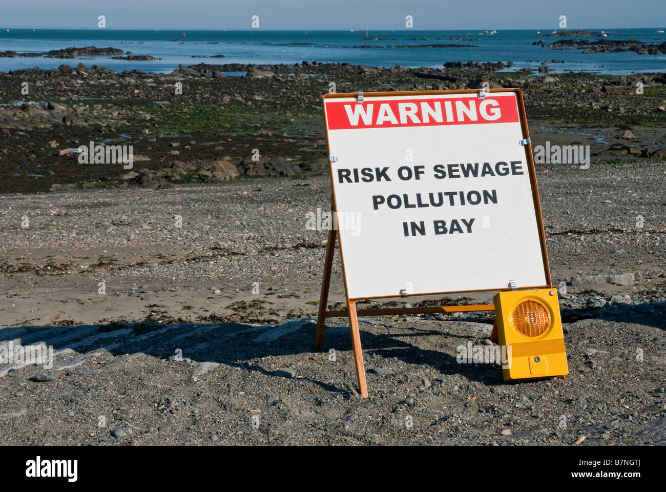 Sign at top of beach warning of sewage pollution in bay. In the
