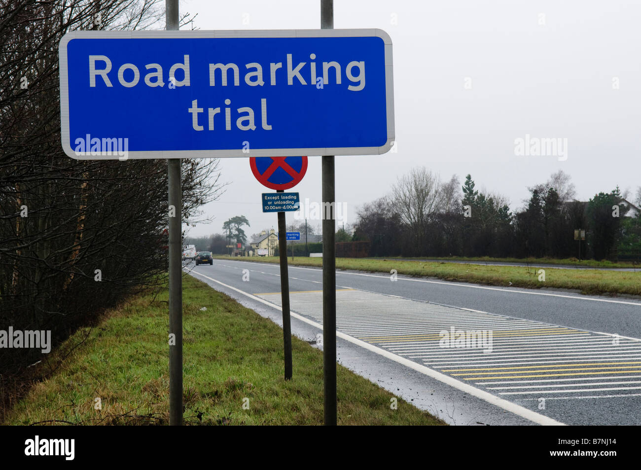 Road sign advising motorists of 'road marking trial', against overcast sky and rain Stock Photo