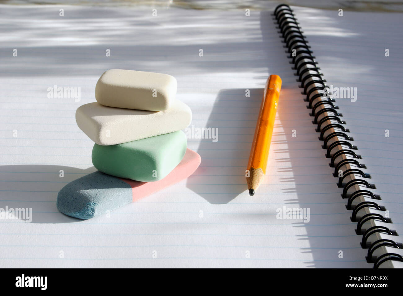 A pile of erasers and a pencil on the page of a spiral exercise book