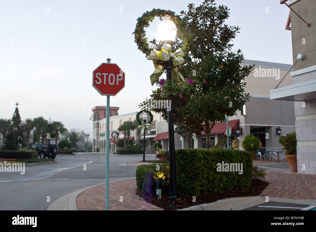 Red stop sign behind an old-fashioned streetlamp decorated with Christmas wreath and ribbon on a sidewalk by a roadway Stock Photo