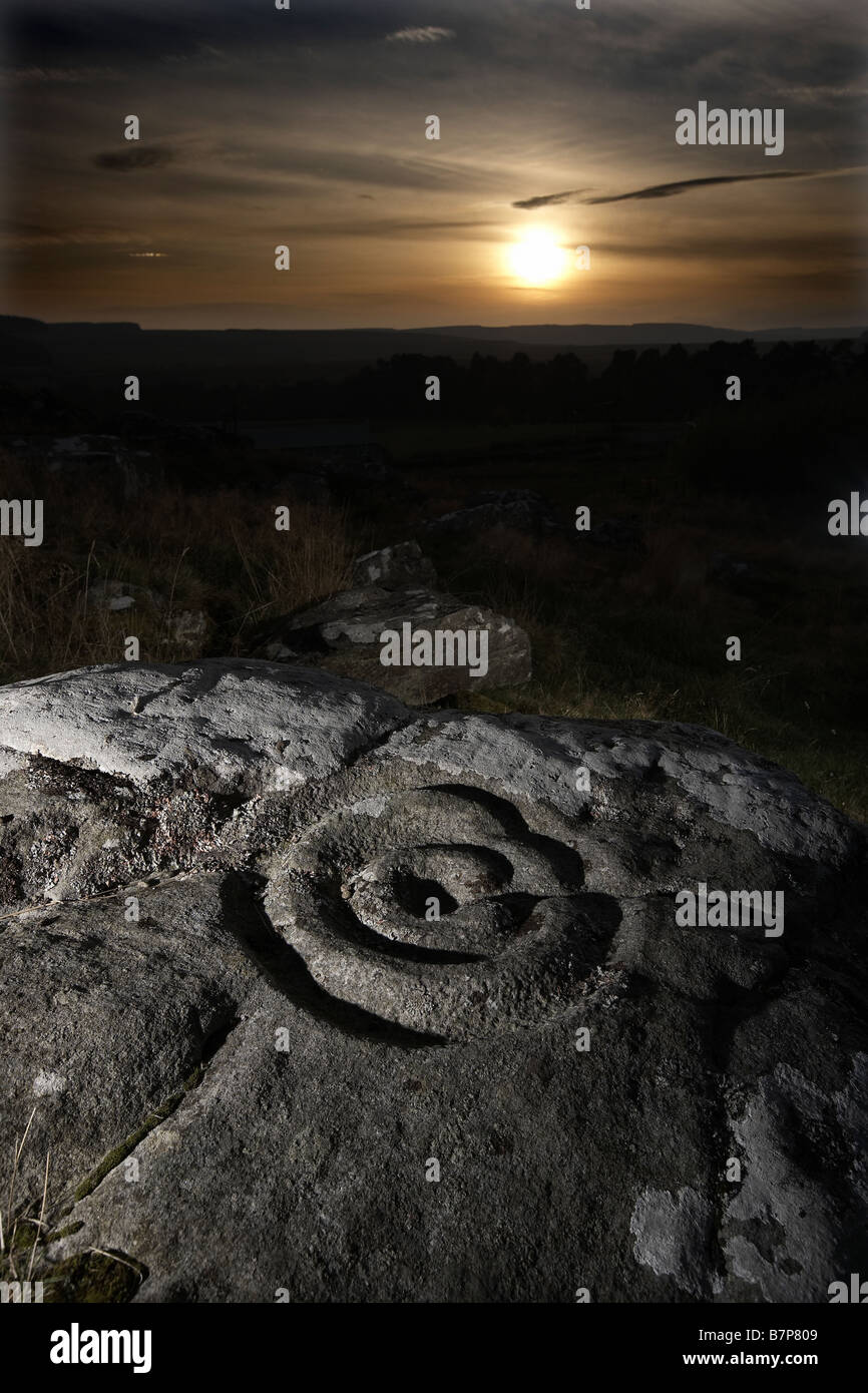 Sun sets over the prehistoric cup and ring marks rock art carved on rock at Brigantium Northumberland England UK Stock Photo
