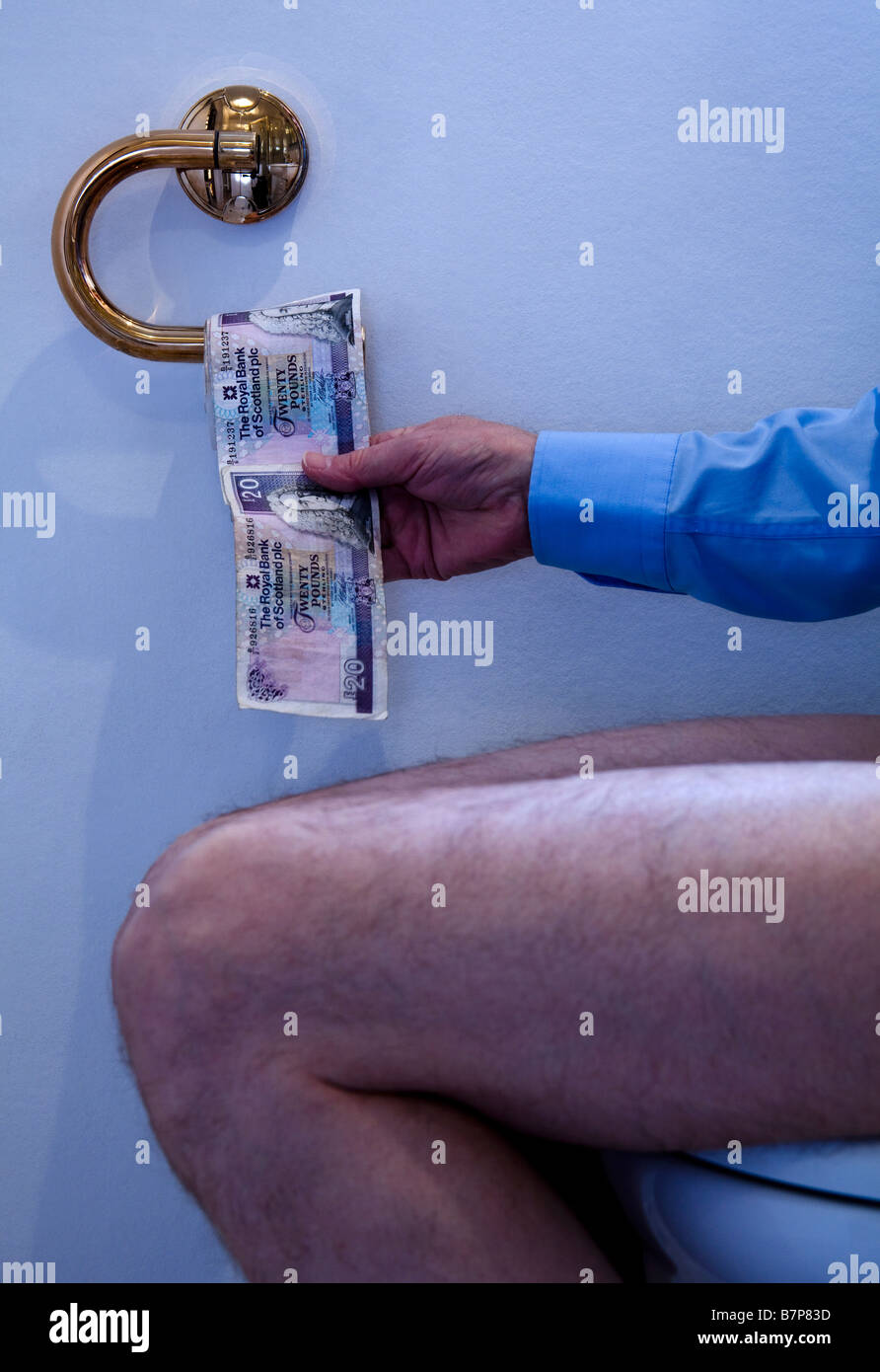 Businessman pulling Roll of £20 Royal Bank of Scotland banknotes, Twenty Pound while sitting on toilet bowl, Scotland, UK, Europ Stock Photo