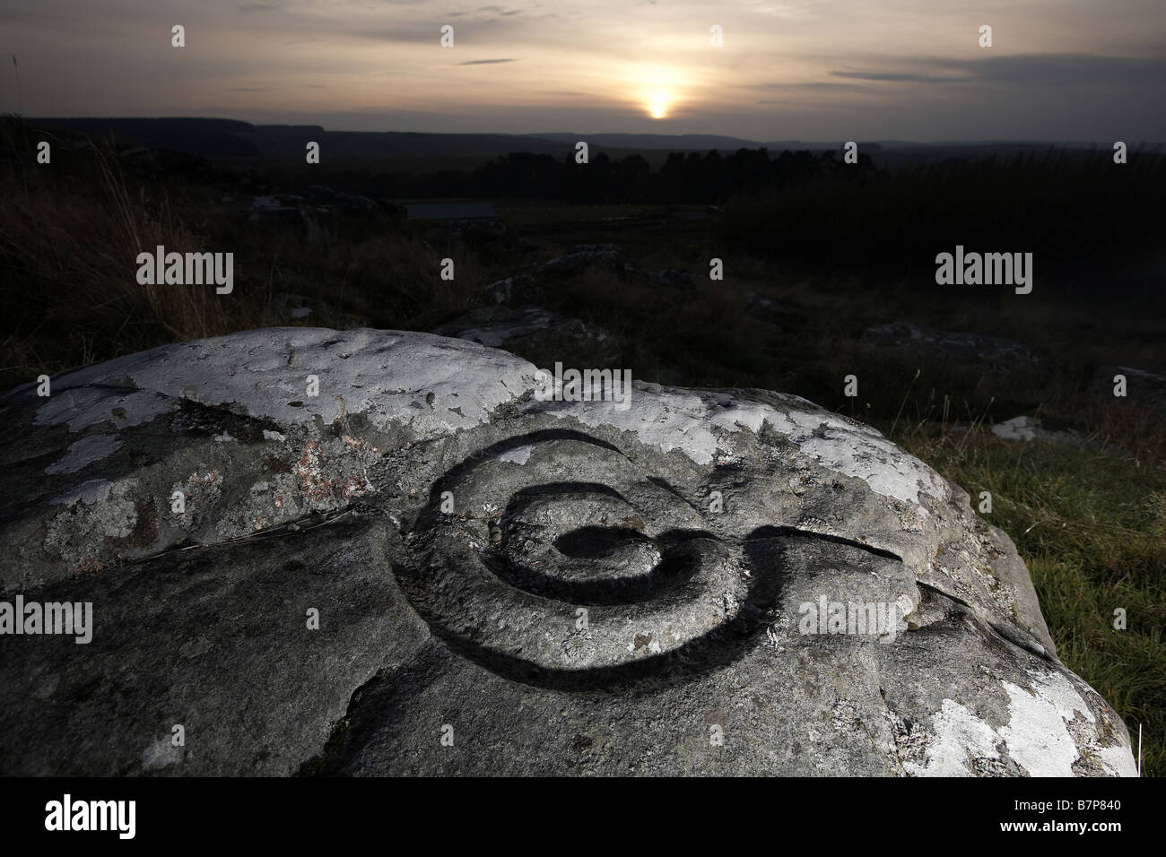 Sun sets over the prehistoric cup and ring marks rock art carved on rock at Brigantium Northumberland England UK Stock Photo
