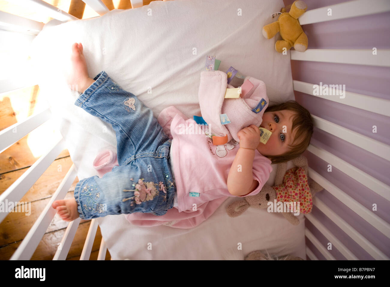 A Baby Girl Lies In Her Cot And Chews On Her Comfort Blanket Stock