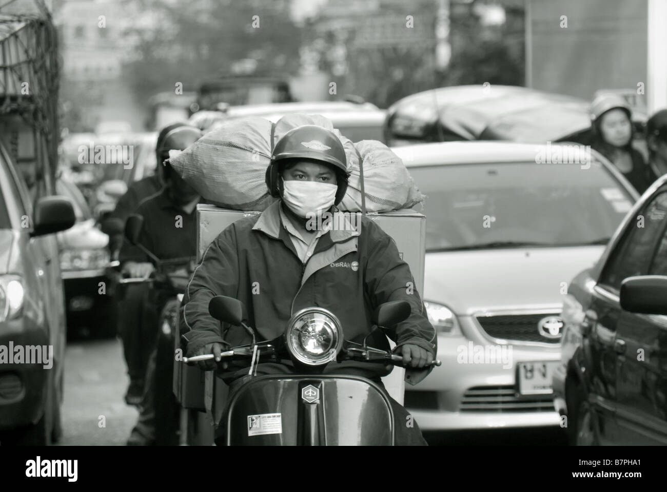 Man riding a scooter wearing a mask against pollution in heavy traffic along Thanon Yaowarat in Chinatown Bangkok Thailand Stock Photo
