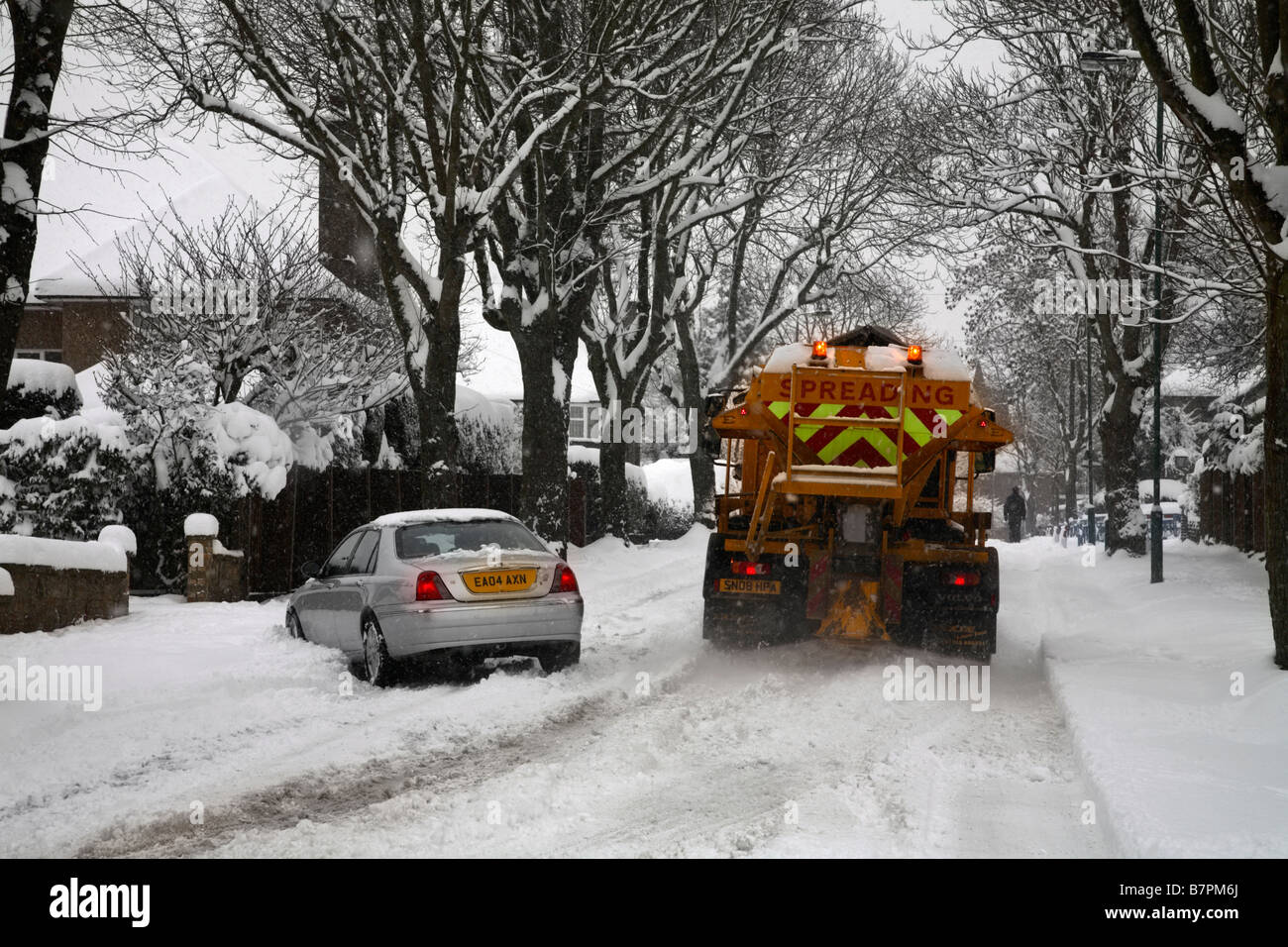 Gritting Lorry grititng snow covered road whilst car slides Cheam Surrey England Stock Photo