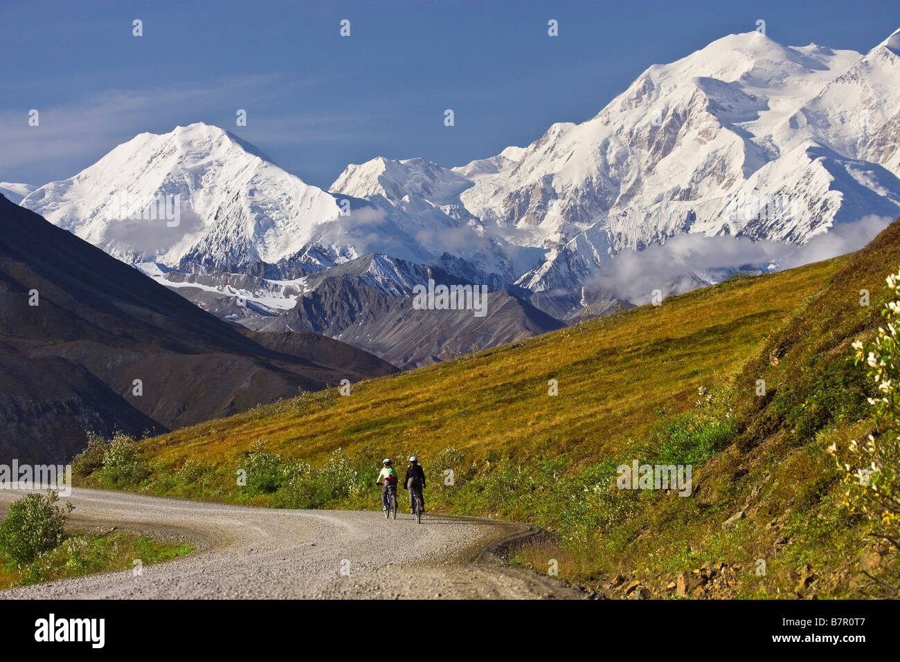 Two women ride bikes over Thorofare Pass with Mt. McKinley in the background in Denali National Park, Alaska Stock Photo