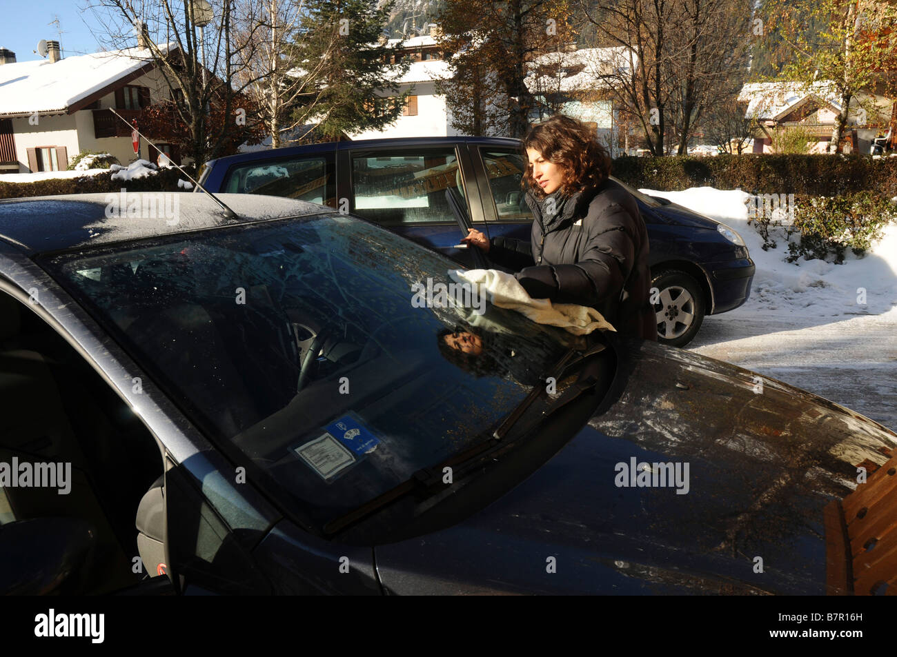 Italy The Dolomites Woman scraping ice off her car s windshield on a cold and frosty morning Model Release Available Stock Photo