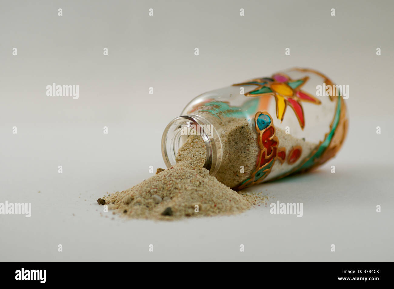 Toppled colourful bottle, spilling sand. Stock Photo