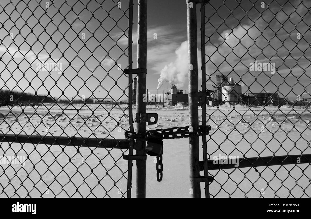 Smoke billowing from the smoke stacks of an oil refinery, pollution and global warming. locked fence, chain links. Stock Photo