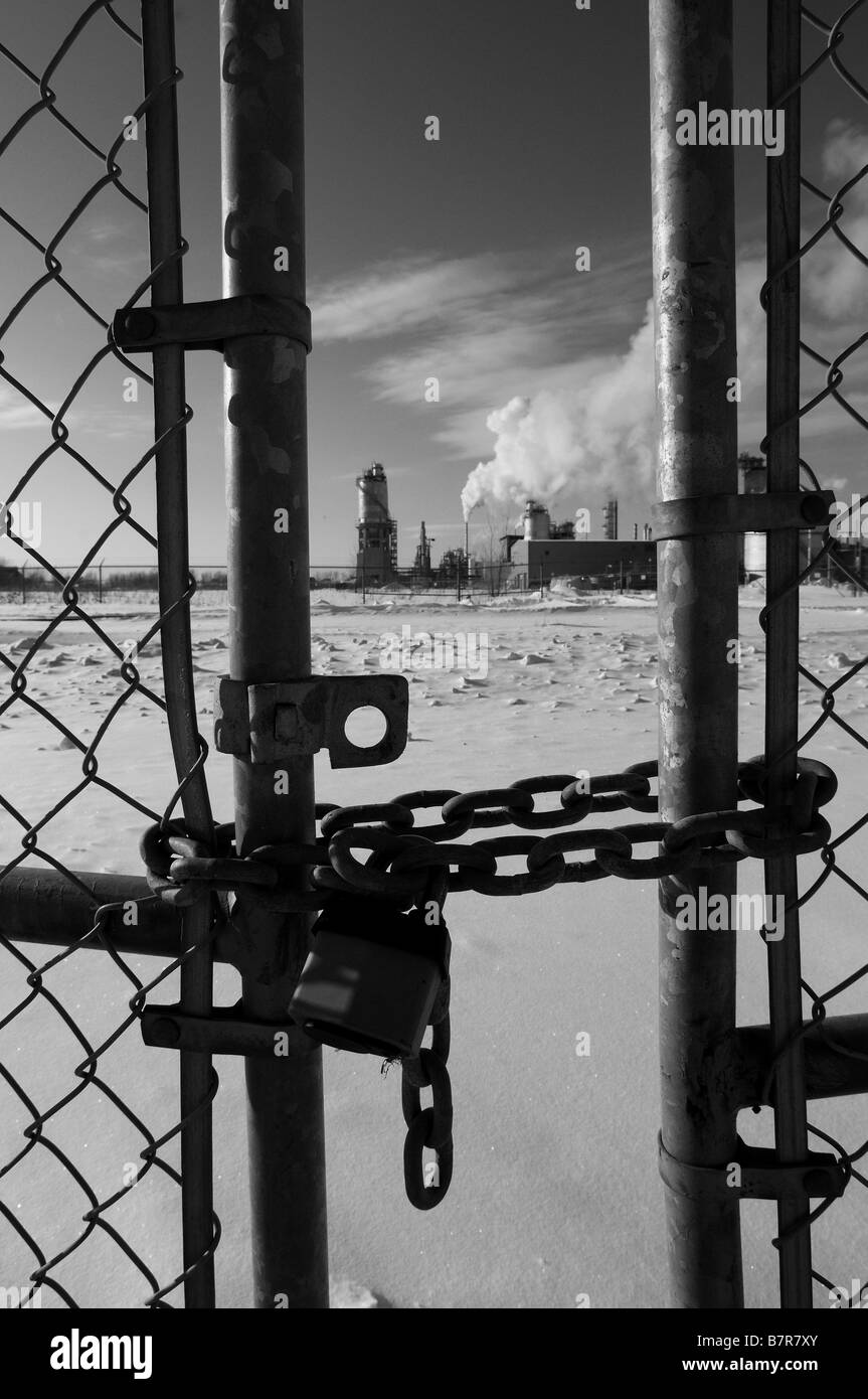 Smoke billowing from the smoke stacks of an oil refinery, pollution and global warming. locked fence, chain links. Stock Photo