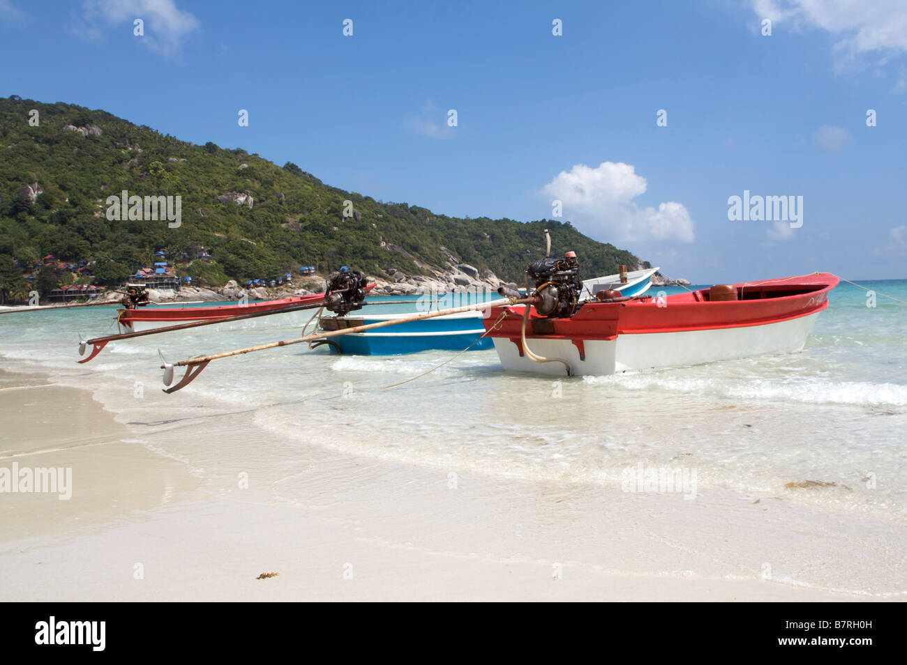 A long tail boats sits on the crystal clear waters of  Haad Rin Nok beach Koh Phangan Thailand under a blue sky Stock Photo