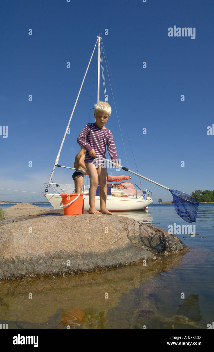 young boys fishing with landing net and sailboat in background Stock Photo