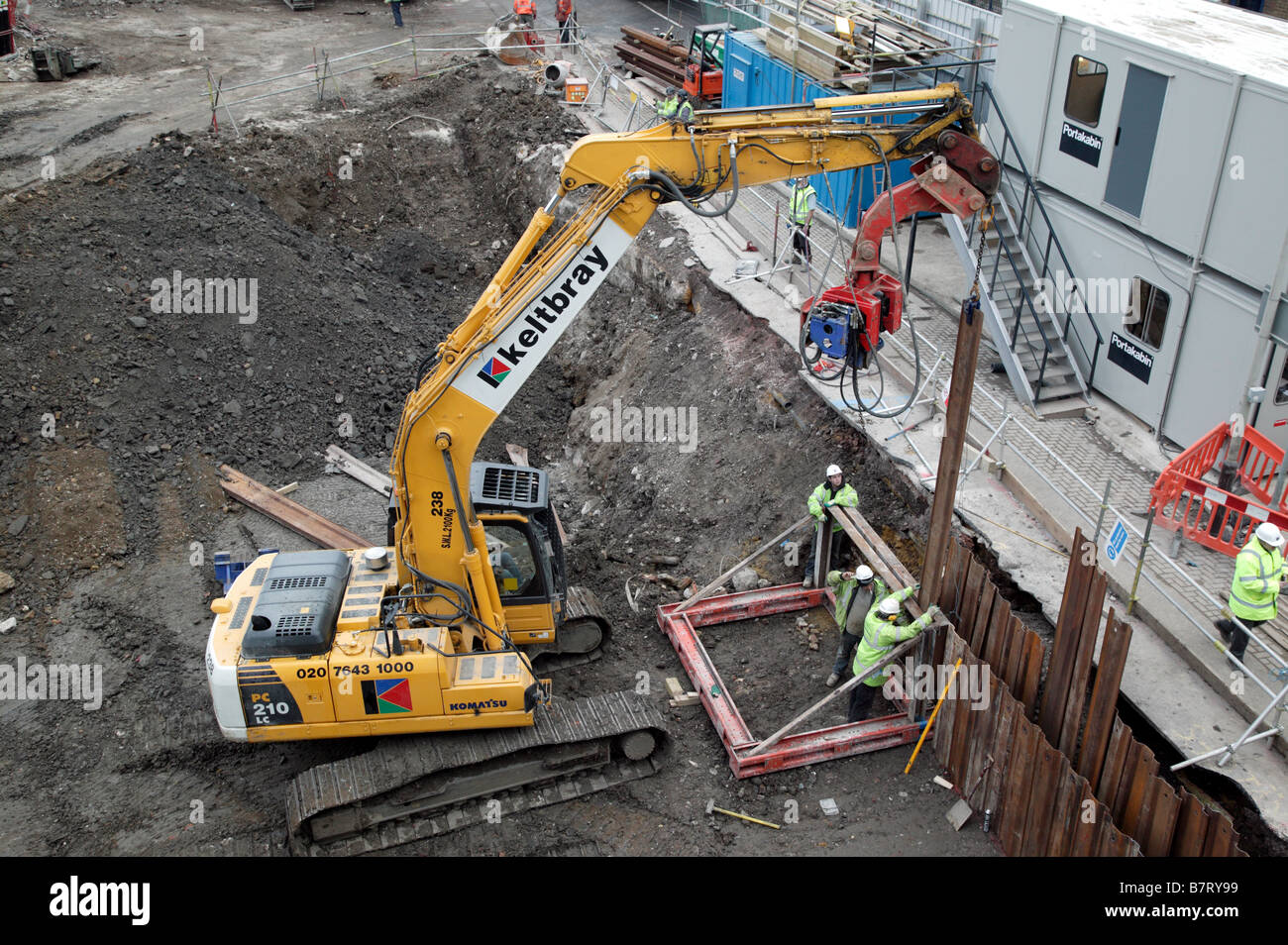 Excavator fitted with a vibratory pile driver maneuvering steel sheet piles into position using a metal Jig Stock Photo