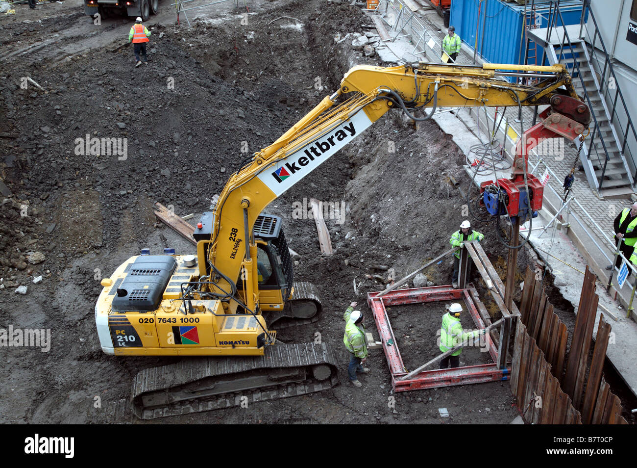 Workman using a vibratory pile driver attached to an excavator to drive in steel piles for  temporary foundation shoring Stock Photo